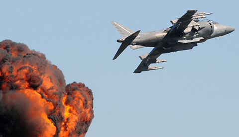 a jet in flight with a ball of flames behind it from a dropped bomb